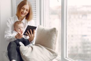 Beautiful woman with child. Woman in a white shirt. Family on a windowsill use the tablet.